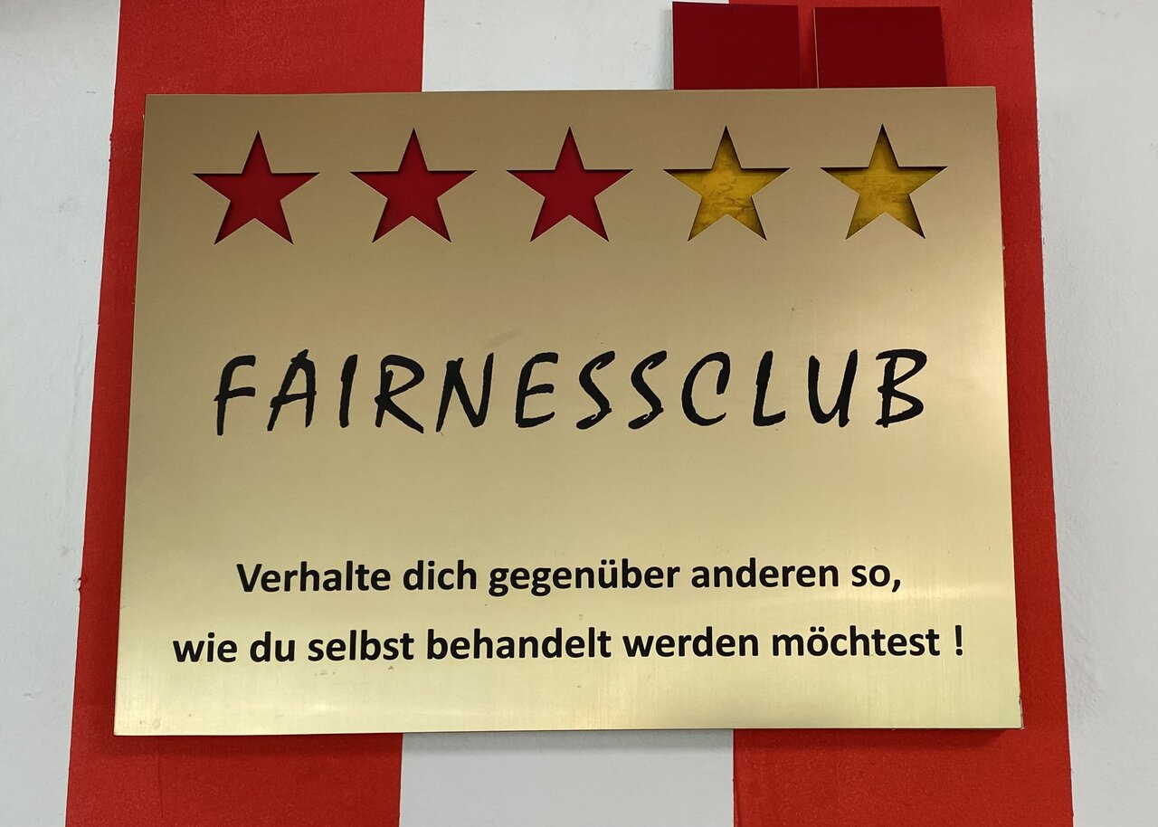 Ein goldenes Schild mit 5 Sternen, drei davon rot ausgefüllt. Es zeigt den Stand des "Fairnessclub" an. Darunter der Spruch "Verhalte dich anderen gegenüber so, wie du selbst behandelt werden möchtest"