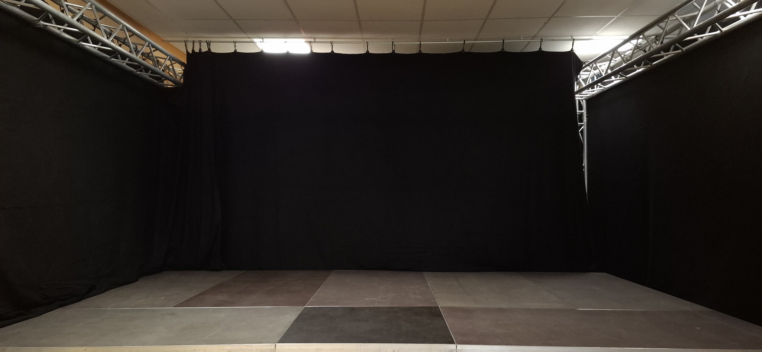 Eine leere Bühne mit schwarzen Vorhängen seitlich und hinten, die dazu einlädt sie zu bespielen