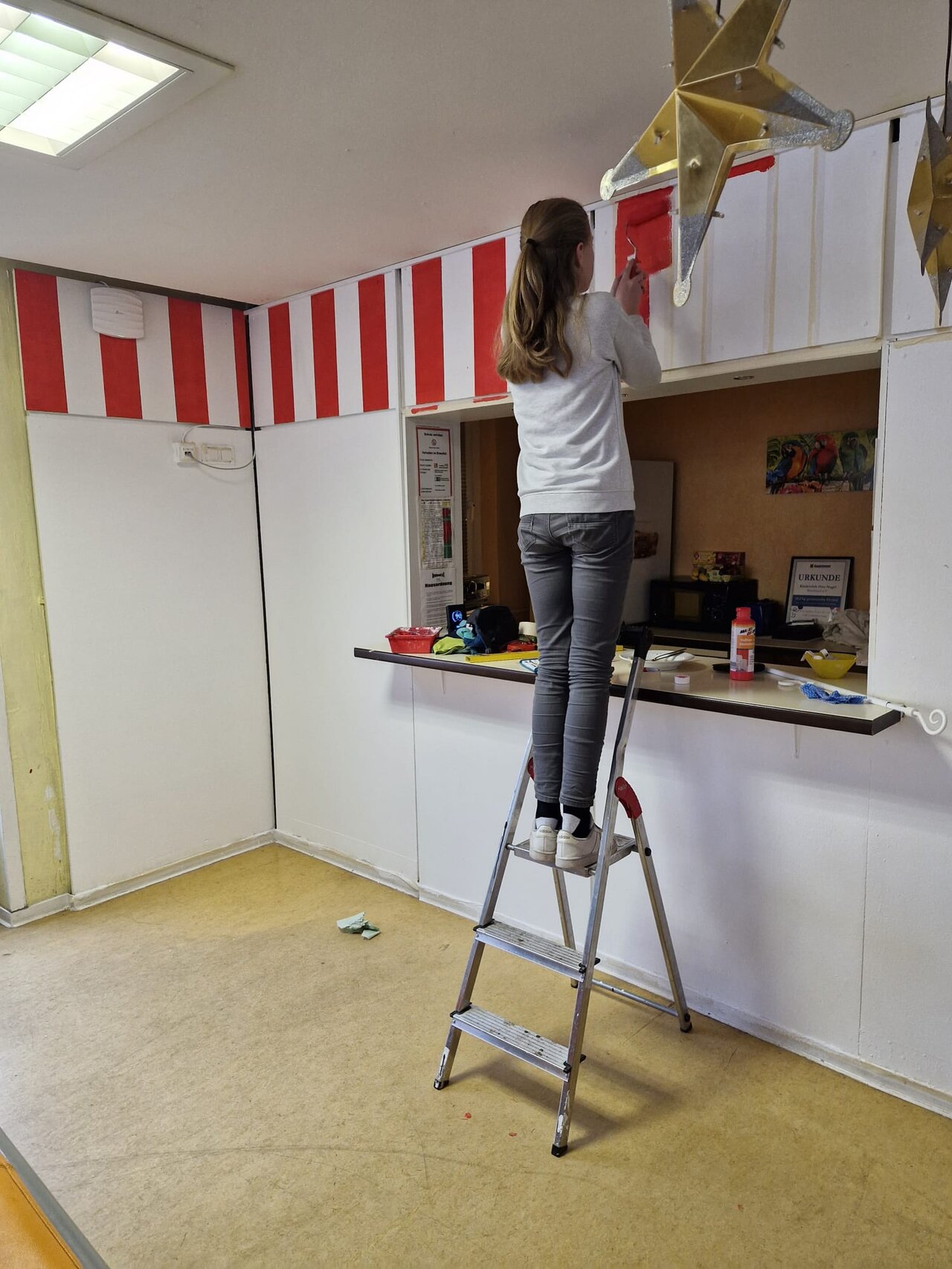 Ein Kind hilft beim malen des neuen Tresenbereichs des ONC, auf einer Leiter stehend.