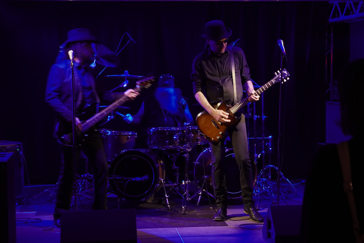Drei Musiker auf der dunkel-blau beleuichteten Bühne im HEK mit Gitarre, Bass und Schlagzeug